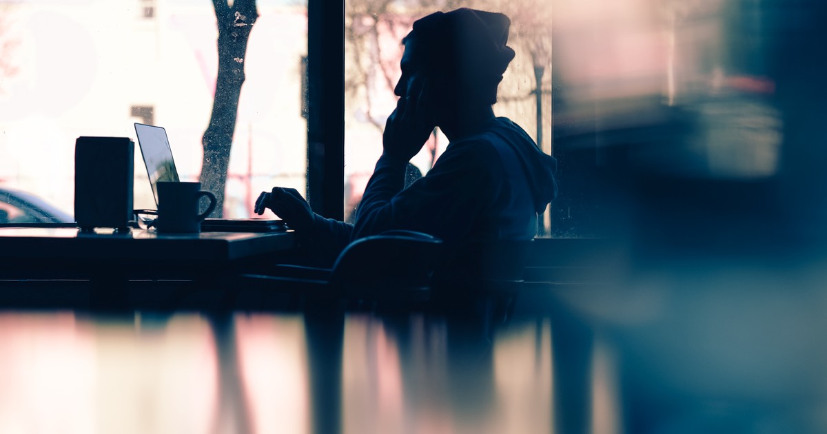 Silhouette of a person writing on a laptop at a cafe window